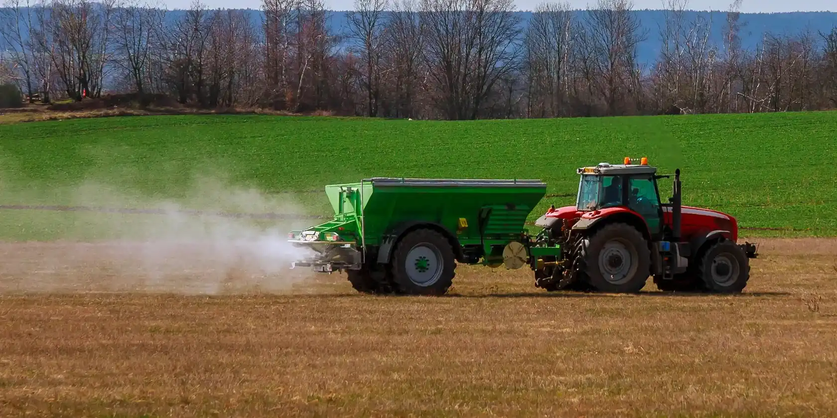 Ciągnik z rozsiewaczem podczas równomiernego wysiewu granulowanego nawozu Bluebird Fertilizers na polu